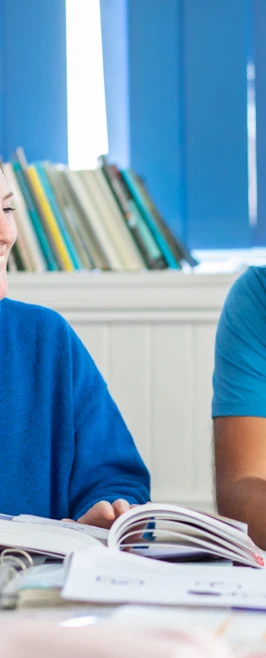 Two students in a Gaelic language class laughing while studying, with a Gaelic-English dictionary open on the desk. Two students in a Gaelic language class laughing while studying, with a Gaelic-English dictionary open on the desk.